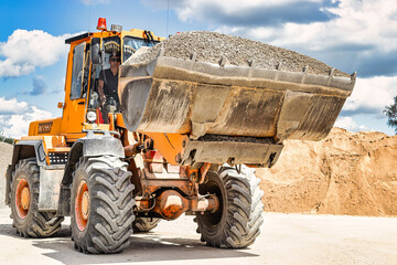 A large front loader transports crushed stone or gravel in a bucket at a construction site or...