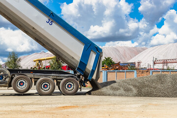 A large dump truck unloads rubble or gravel at a construction site. Car tonar for transportation of heavy bulk cargo. Providing the construction site with materials.