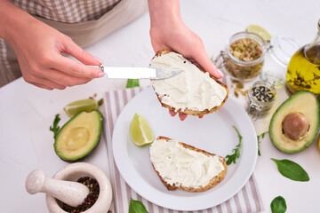 Obraz na płótnie Canvas Avocado and cream cheese toasts preparation - Woman smearing cheese on a grilled or toasted bread