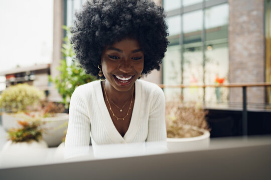 Smiling young african woman sitting with laptop in coffee shop