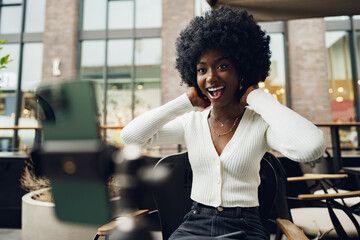 Portrait of smiling woman with afro hairstyle on video call sitting in cafe