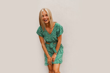 Laughing blond woman in green stylish summer dress posing ower white wall.