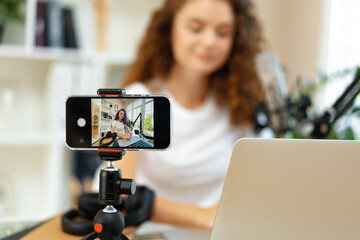 Young curly female blogger recording video at table at home
