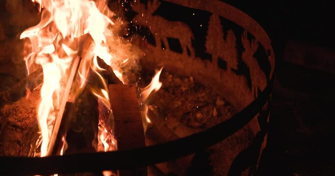 Slow motion of a person putting in a log to keep the fire going.