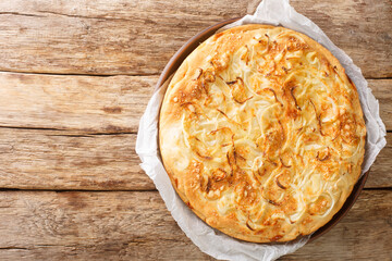 Fugazzeta is a scrumptious cheese stuffed pizza topped with caramelized onions from Argentina closeup in the plate on the wooden table. Horizontal top view from above