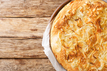 Fugazzeta pizza with onions and mozzarella on a thick crust closeup in the plate on the wooden table. Horizontal top view from above