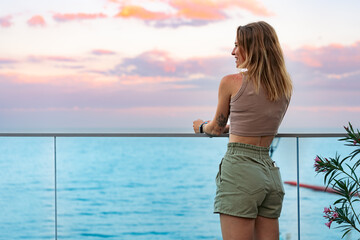 Beautiful young woman standing and looking at the sea and sky