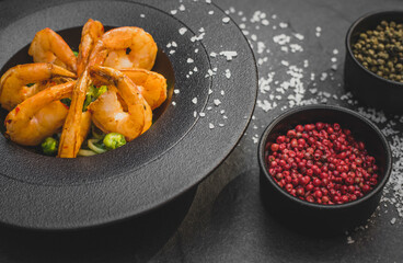 Cooked shrimp in a round shaped black dish. Seafood on a plate. Decorated with salt. Black Stone table. 