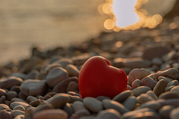 Valentine's Day concept. Red heart romantic love symbol on pebble beach at sunset with copy space....