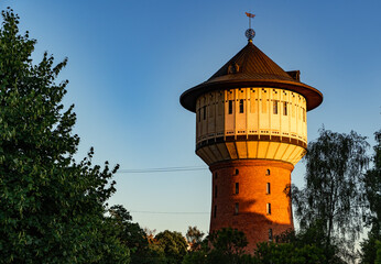 Old red brick water tower surrounded in trees in sunset light