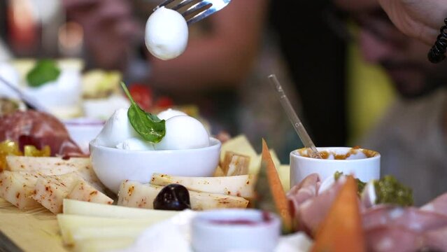 Restaurant Gastronomy Dinner Buffet and Aperitif, Hors D'oeuvre and Assortment of Various Appetizers, Mozzarella Cheese Prosciutto, Blurred Background Woman's Hand Takes Piece of Mozzarella with Fork