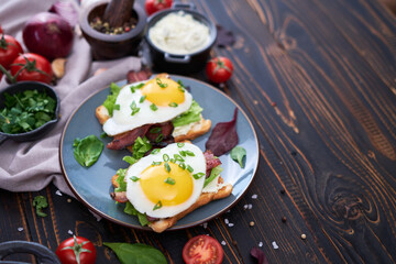Fried eggs, bacon and cream cheese sandwiches on a plate on wooden table at domestic kitchen