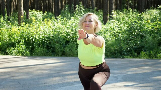 Middle-aged blonde lady makes body stretching exercises on sports ground. Lady does yoga training in city park. Sportive woman enjoys healthy living