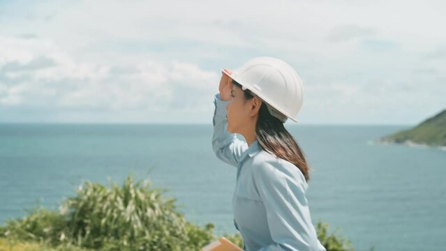 a woman engineer is walking in a field wearing a protective helmet on her head