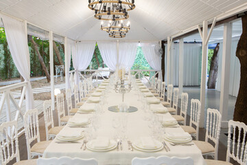 Empty banquet hall ready to receive guests on the summer terrace. white festive table