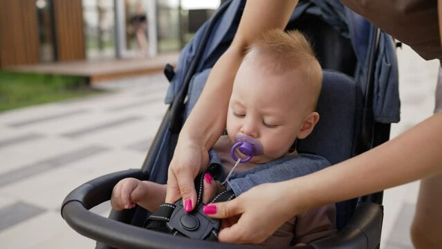 A little boy is strapped into a wheelchair. Attachments for baby strollers. Mom fastens the baby in the stroller. Mom fastens the baby in the stroller for safety on a summer day.