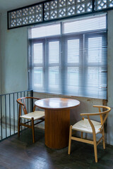 The wooden table and chairs near the window in cafe with sunlight through the window blind sunshade. Empty chairs and table with light and shadow in the room.