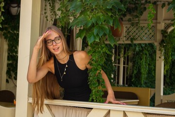 blonde girl in a black dress and glasses looks out of the gazebo