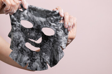 Female hands holding sheet of black bubble mask on pink background.