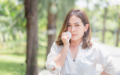 Young pretty girl drying sweat using tissue on a warm summer day in a park, Woman in the park...