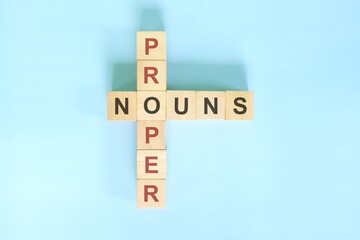 Proper nouns concept in English grammar education. Wooden block crossword puzzle flat lay in blue background.	