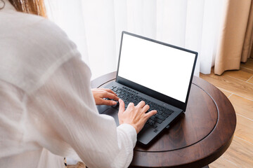 Fototapeta premium Person working at a laptop, close-up of hands and computer screen, remote work on a light background.
