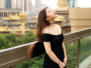 Portrait of beautiful Chinese young girl wearing black tube dress posing with eyes closed with Shanghai landmarks background, outdoor fashion portrait of glamour sexy stylish lady with black long hair