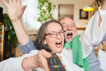 Paar Senioren mit TV Fernbedienung jubelt glücklich