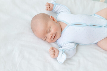 smiling or laughing in a dream, a newborn baby boy sleeps for seven days in a cot at home on a cotton bed, close-up