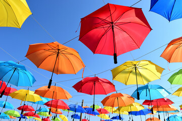 Fototapeta na wymiar colorful parasol sun protection. bright umbrellas suspended overhead on metal wires. climate change and global warming concept. summer travel tourism and vacation theme. design and urban environment. 
