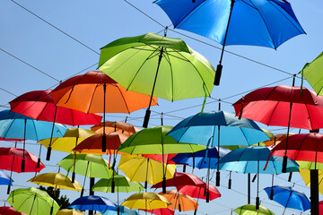 Obraz na płótnie Canvas colorful parasol sun protection. bright umbrellas suspended overhead on metal wires. climate change and global warming concept. summer travel tourism and vacation theme. design and urban environment. 