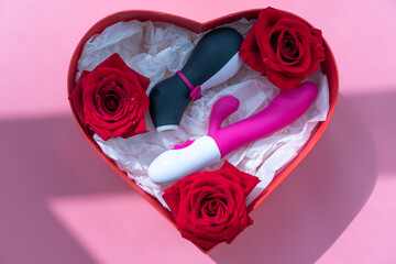 Satisfyer pro penguin, the most famous dildo for women and a pink vibrator in a heart shaped gift box on a pink background. Shadow from the window. Gift concept for adults from online sex shop.  - obrazy, fototapety, plakaty
