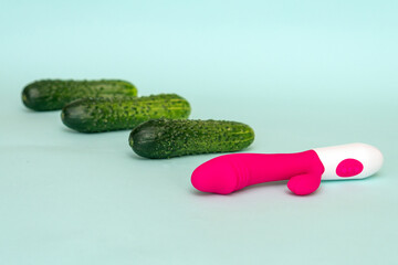 Pink dildo and green cucumbers on a blue background. Focus on vibrator