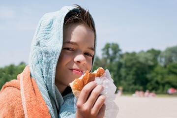 A little boy eats a sandwich after swimming