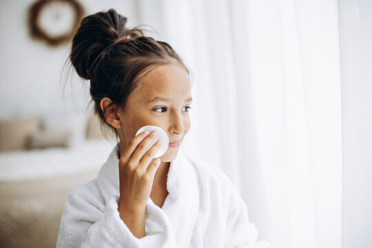 Girl cleaning her face using cotton pad