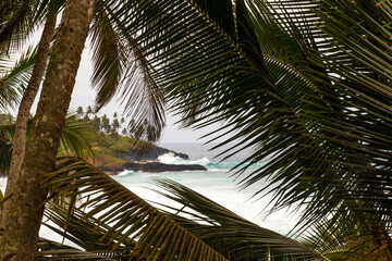 Crashing waves of the Boca d'Inferno framed by palm leaves, along the coastline of the tropical...