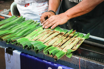 Thai sweetmeat made from flour, coconut and sugar and wrapped with palm leaves on charcoal stove.