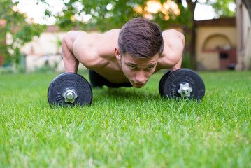 Young strong man doing pushups on the backyard grass in summer