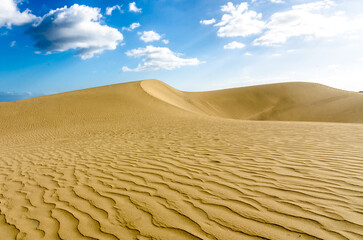 Desert sand dunes in sunlight with cloudy sky in background