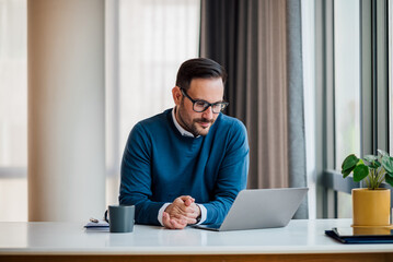 Fototapeta premium Confident smiling manager looking at laptop while sitting at the desk in the office.