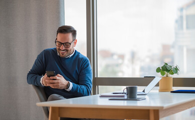 Smiling entrepreneur socializing on smart phone while working at the office desk.