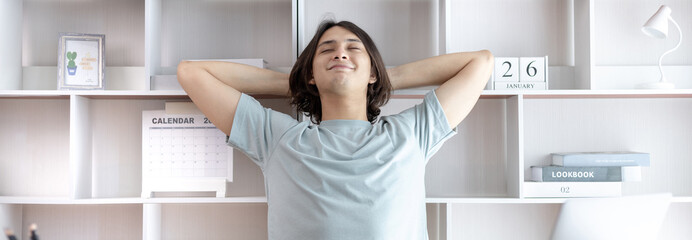 Young Asian male employee is doing a relaxing posture after a hard Midday's work, Happy men resting at work after work is finished, Fatigue is eased, Men working at home, Relax, Attractive, Success.