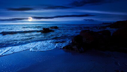 huge stones on the sandy beach at night. wonderful velvet season vacation on the black sea in full moon light. calm waves washing the shore. clouds on the dark blue sky above horizon
