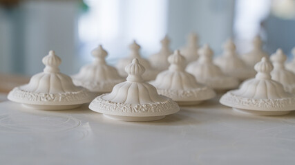 A group of porcelain lids for the tea pot, dry on pallets before glazing and firing. Shallow depth of field.
