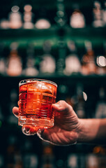 man hand holding a glass of negroni cocktail in a bar