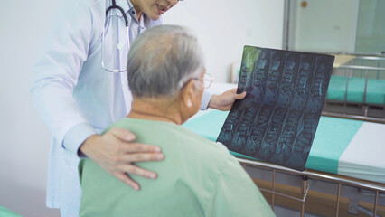 Portrait of Asian doctor showing bone x-ray scan film of sick old senior elderly patient on bed in hospital in medical and healthcare treatment at nursing home. People lifestyle