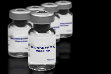 Monkeypox vaccine close-up on a black mirror background. In the background are blurred vaccine vials.