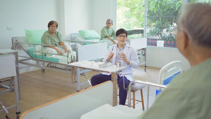 An Asian doctor talking to group of old elderly patient or pensioner talking, have a meeting, in nursing home in hospital. Senior people lifestyle activity recreation. Health care physical therapy.