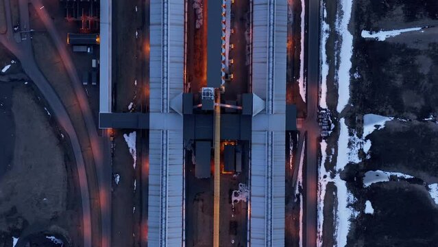 Top down above long aluminium production building with night lights on, aerial