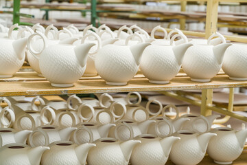 A group of porcelain kettles for infusing tea, dry on pallets before glazing and firing.